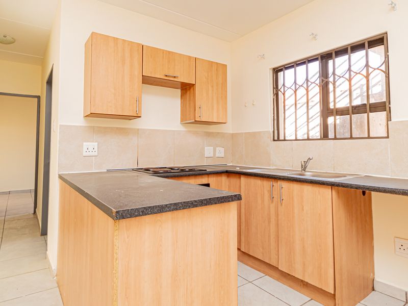 A functional kitchen featuring laminate cabinetry, dark countertops, a built-in hob, and a stainless steel sink, with tiled flooring and a security-barred window.