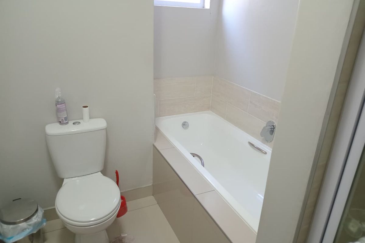 A clean and functional bathroom featuring a built-in bathtub with tiled splashback and a standard toilet.
