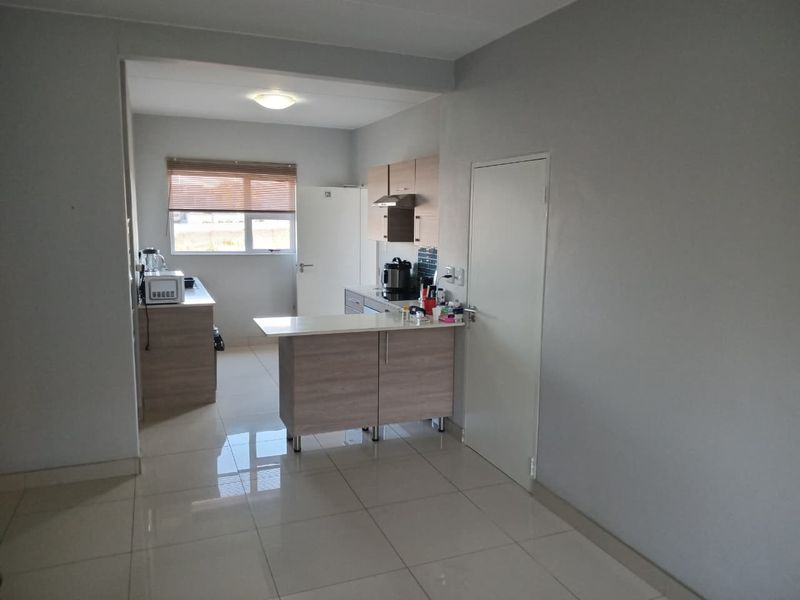 An open-plan kitchen area featuring modern light wood cabinetry, a breakfast bar, and tiled flooring, providing a functional and bright living space.