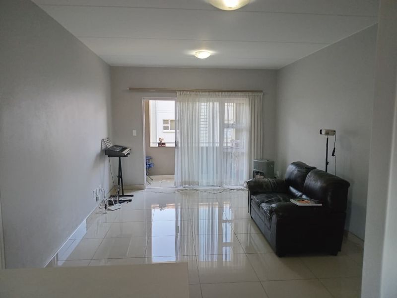 A bright living room featuring polished tiled flooring and a large sliding glass door providing access to an attached balcony.