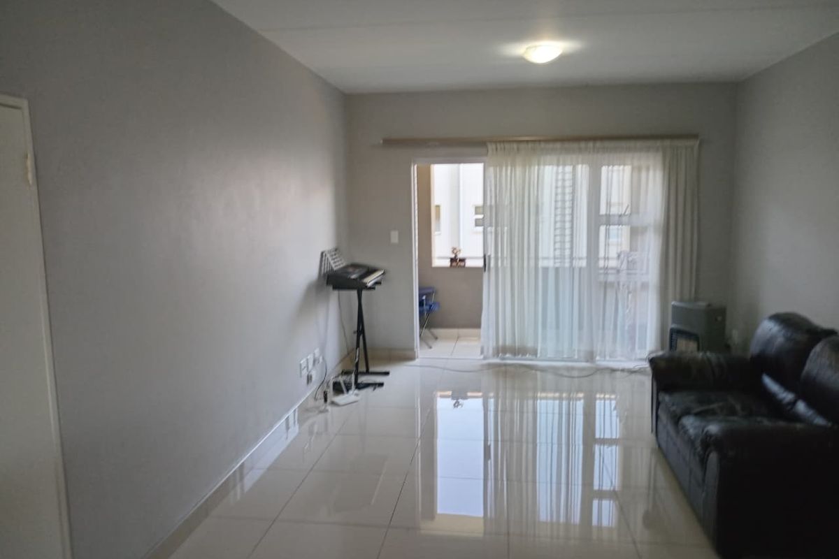A bright living room featuring polished tiled flooring and a sliding glass door leading to an outdoor balcony area.