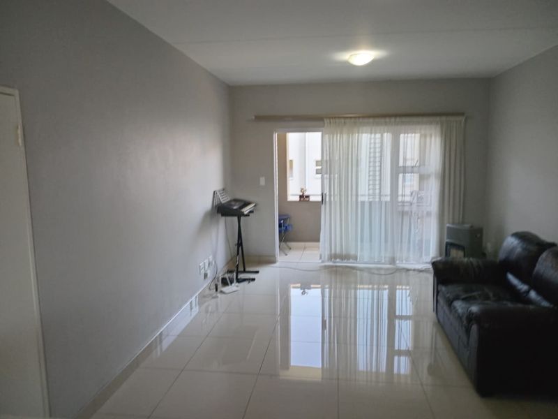 A bright living room featuring polished tiled flooring and a sliding glass door leading to an outdoor balcony area.