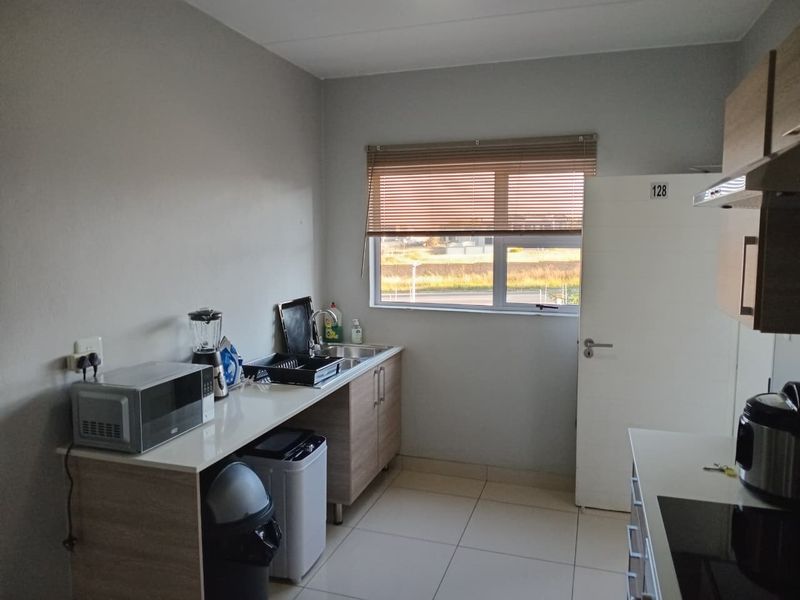 A functional kitchen featuring light wood-finish cabinetry, tiled flooring, a stainless steel sink, and a window with venetian blinds providing natural light.