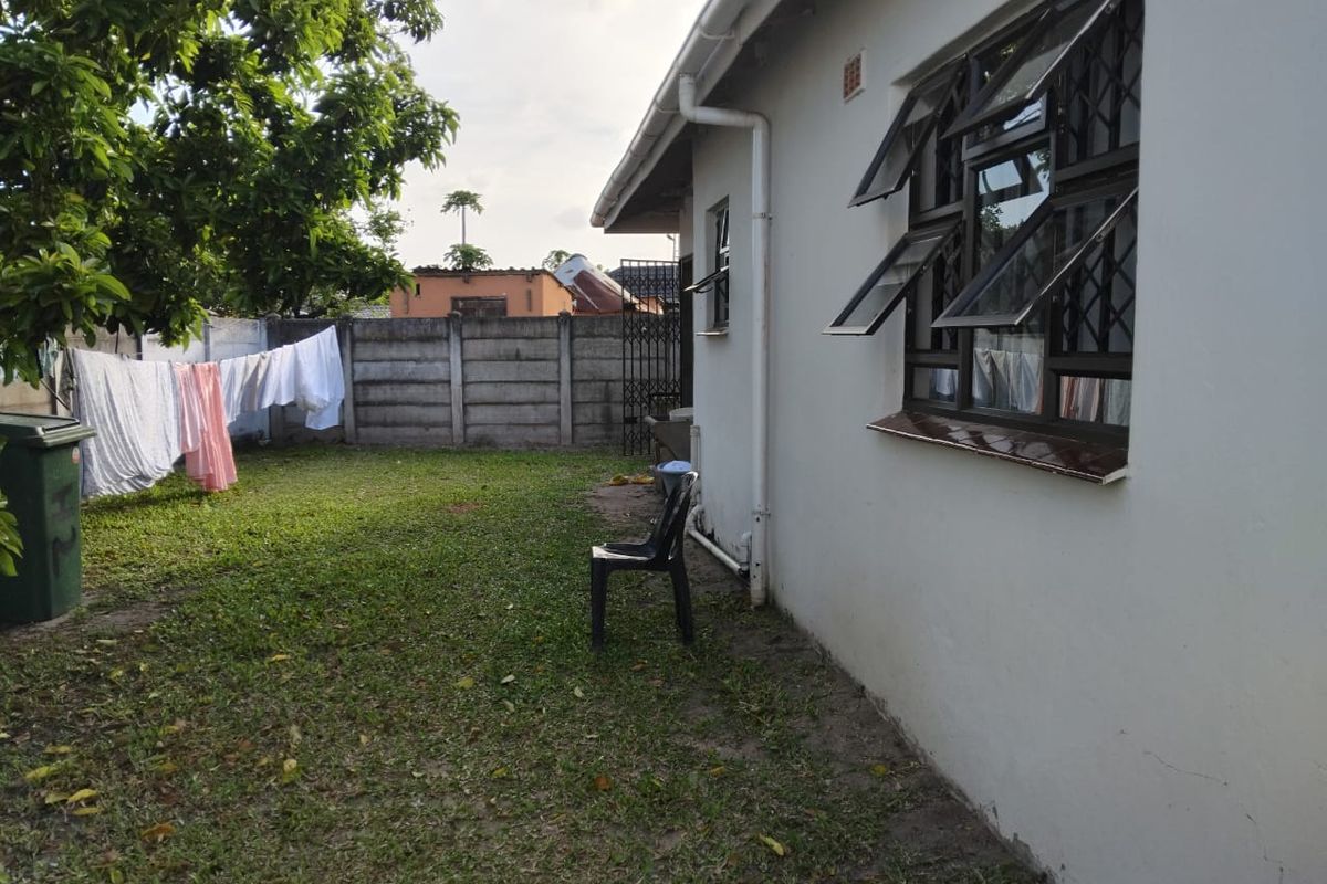 A view of the rear garden area featuring a lawn, perimeter concrete walling, and the side elevation of the house with security-fitted windows.