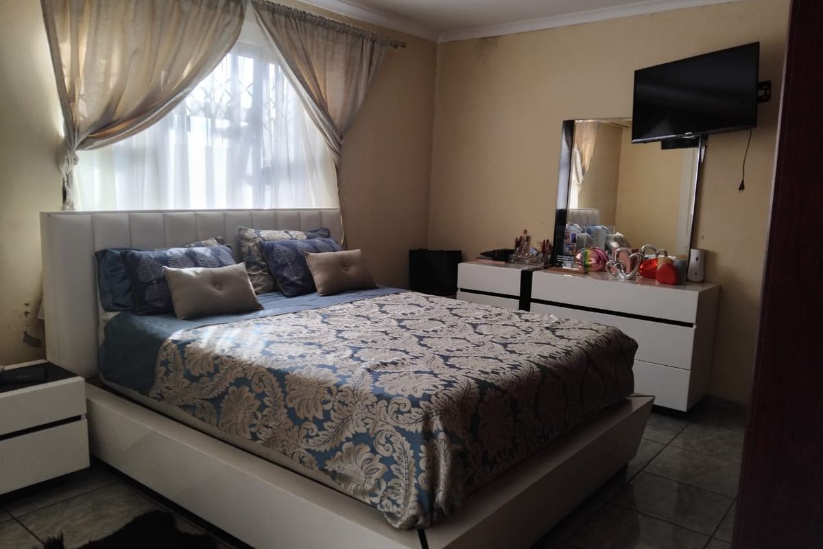 A bedroom featuring tiled flooring and a window with security bars, providing a functional space for rest.