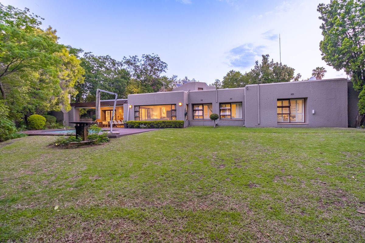 Rear view of the property featuring a spacious lawn, swimming pool, wooden deck, and large windows providing a seamless connection to the garden.