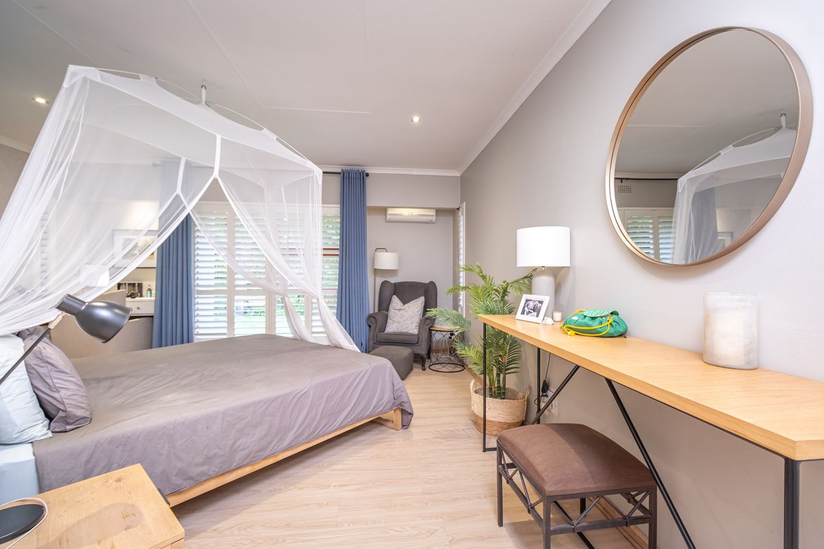 A well-maintained bedroom featuring laminate flooring, recessed downlights, a split-system air conditioner, and plantation shutters for light control.