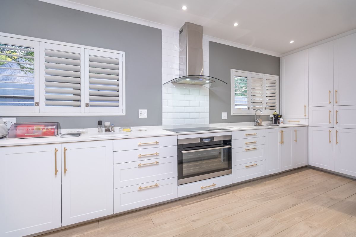 Modern, well-appointed kitchen featuring white shaker cabinetry, quartz countertops, subway tile backsplash, integrated appliances, and plantation shutters.