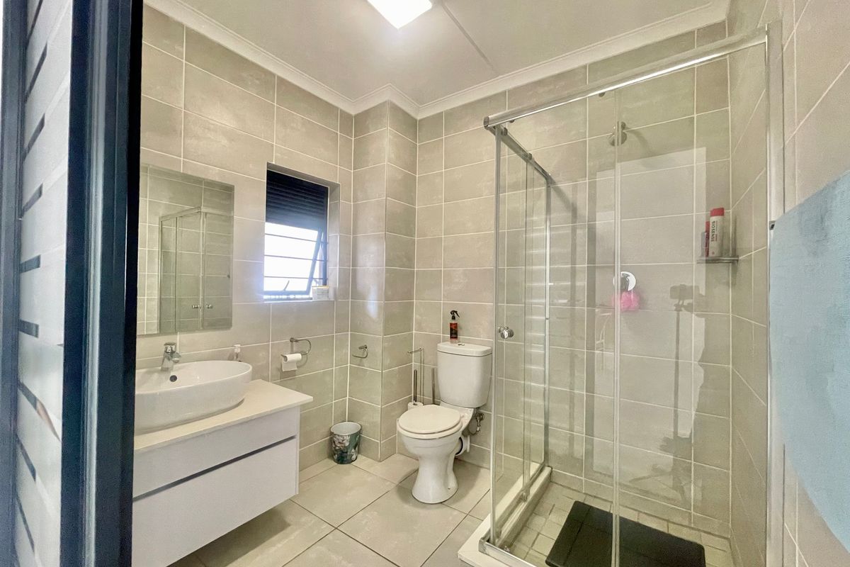 A modern, well-maintained bathroom featuring a vanity cabinet, ceramic basin, glass shower enclosure, and neutral floor-to-ceiling tiling.