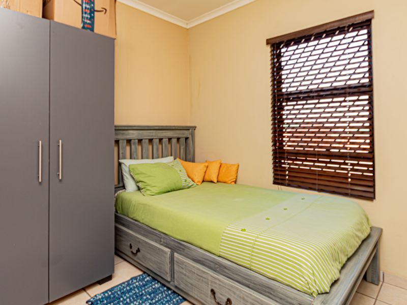 A functional bedroom featuring tiled flooring, neutral wall paint, and fitted venetian blinds, offering a practical space for rest.