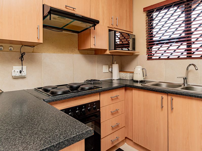 A functional kitchen featuring laminate cabinetry, dark countertops, an electric hob with extractor fan, and a stainless steel double sink with tiled splashback.