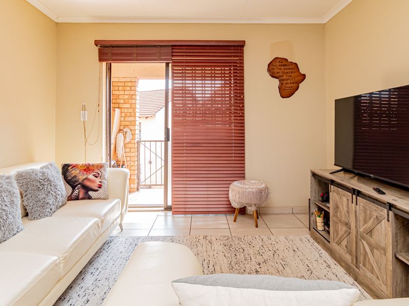 A comfortable living room featuring ceramic floor tiles and a sliding glass door that opens onto a balcony with venetian blinds.