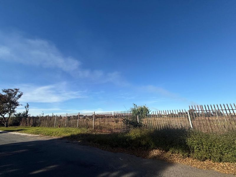 A street-level view of a vacant plot of land enclosed by weathered metal security fencing.