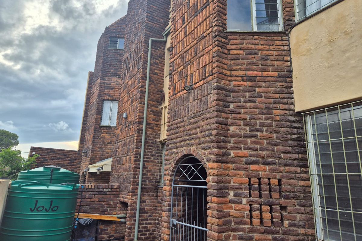 Rear exterior view of a face brick townhouse featuring security gates, window bars, and installed water storage tanks.