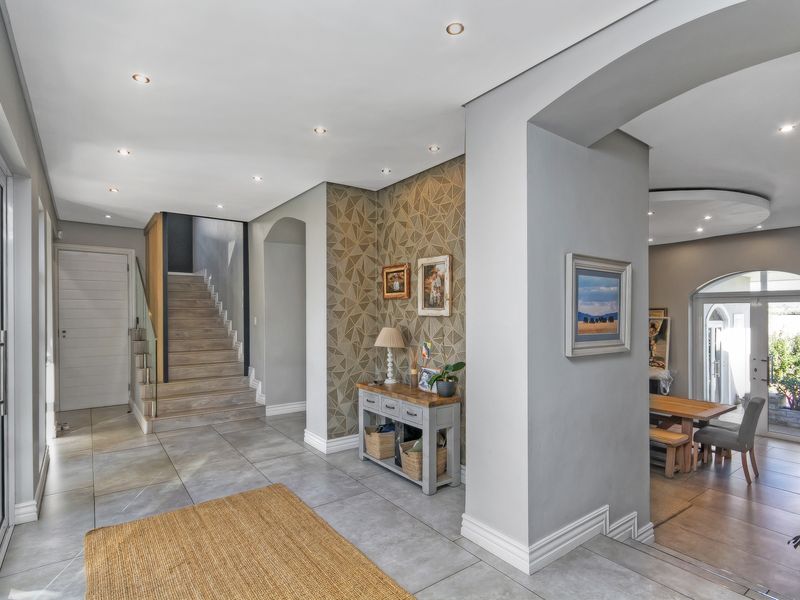 Spacious modern entrance hall featuring tiled flooring, recessed lighting, and an elegant staircase with a glass balustrade, leading into an open-plan living area.