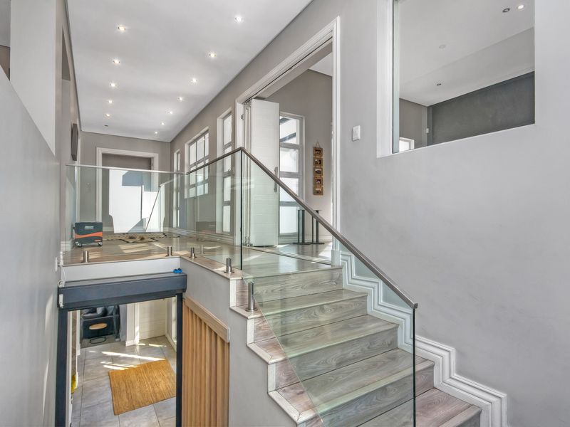 Modern hallway featuring a timber staircase with a sleek glass balustrade, recessed downlighting, and clean architectural lines.