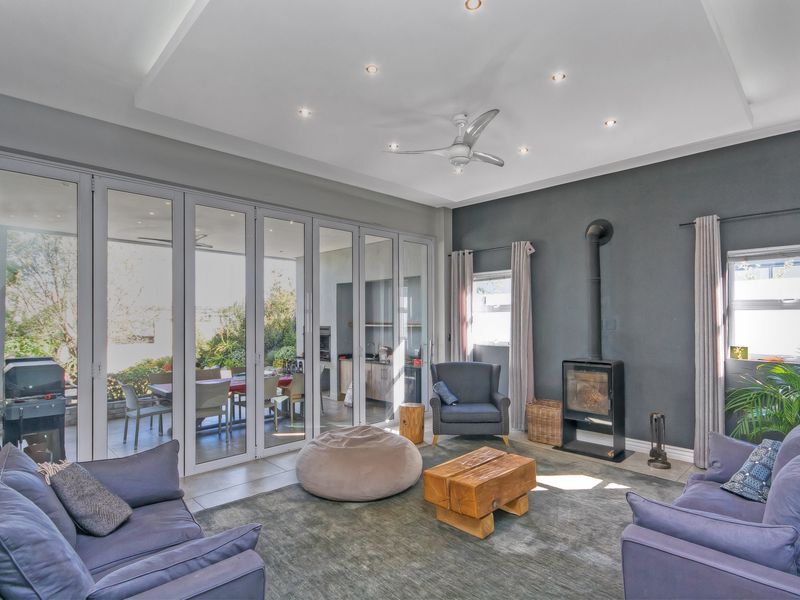 Spacious living room featuring a modern recessed ceiling, downlights, a sleek freestanding fireplace, and large bi-fold glass doors opening to an outdoor patio area.