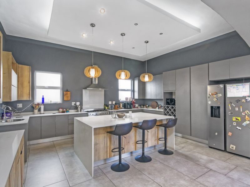 Modern kitchen featuring a large central island with breakfast bar seating, sleek grey cabinetry, quartz countertops, and high-end integrated appliances.