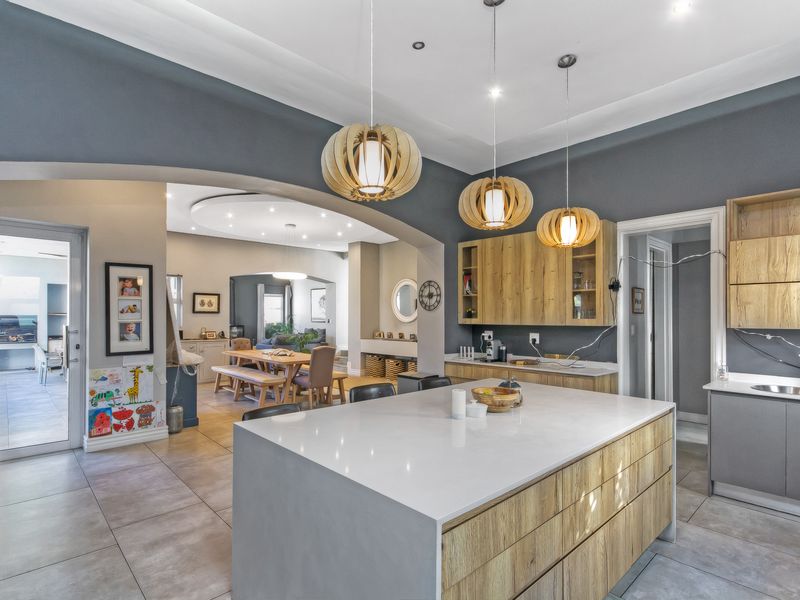 Spacious open-plan kitchen and dining area featuring modern wood-toned cabinetry, stone-topped island, and elegant pendant lighting, flowing into a bright living space.