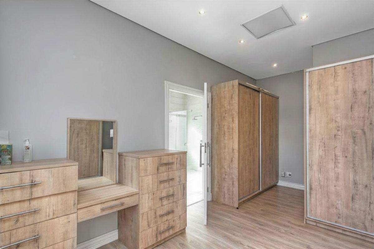 A well-maintained bedroom featuring modern wood-look laminate flooring, built-in cupboards, and recessed ceiling lighting, with direct access to an en-suite bathroom.