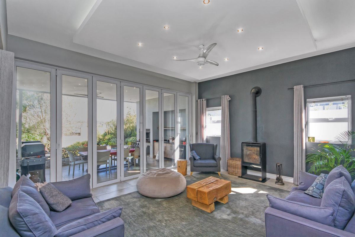 Spacious living room featuring a modern recessed ceiling, downlights, a sleek freestanding fireplace, and large bi-fold glass doors opening to an outdoor patio area.