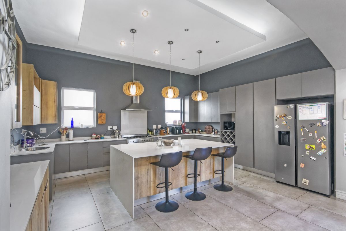 Modern kitchen featuring a large central island with breakfast bar seating, sleek grey cabinetry, quartz countertops, and high-end integrated appliances.