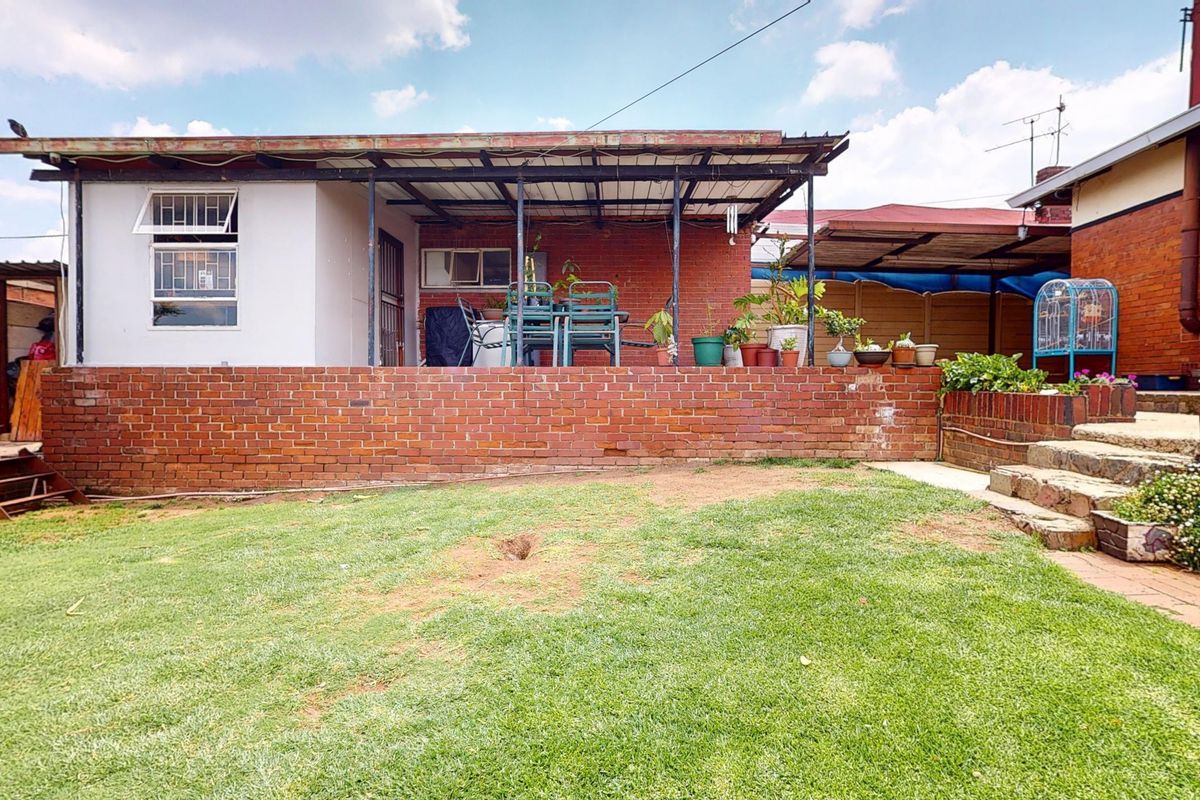 Rear view of the property featuring a brick retaining wall, a covered patio area, and a grassed garden space.