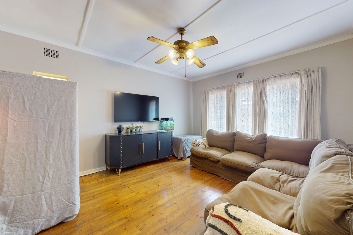 A living room featuring original hardwood flooring, a ceiling fan, and coved ceilings, offering a comfortable and functional space.