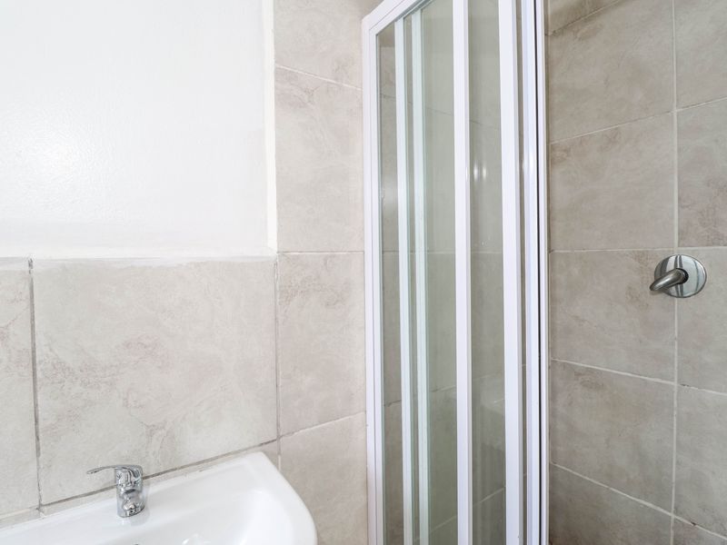 A clean bathroom featuring a shower enclosure with a white frame, neutral ceramic wall tiles, and a modern basin with a chrome mixer tap.