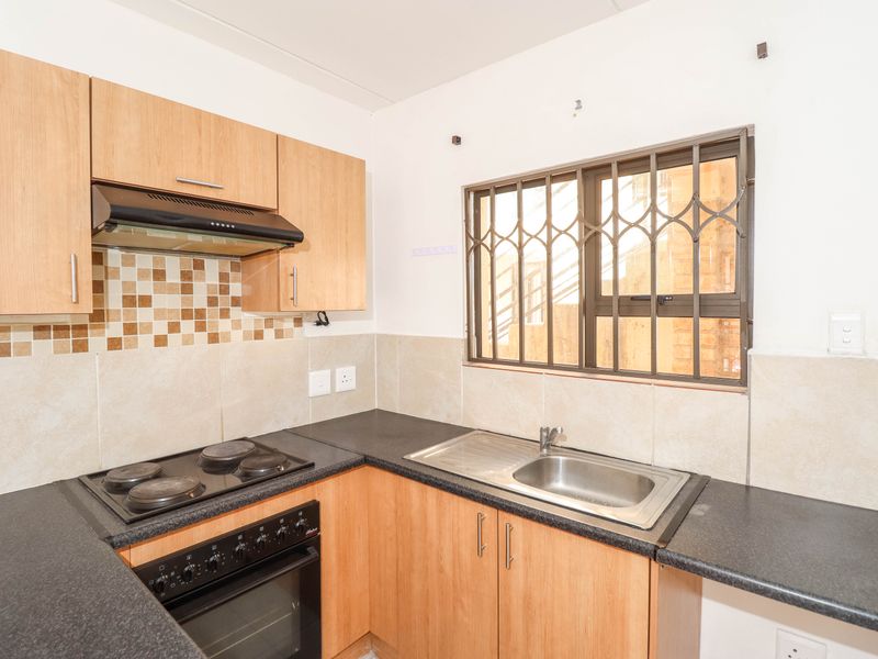 A functional kitchen featuring laminate cabinetry, dark countertops, a built-in oven with hob, and a window fitted with security bars.