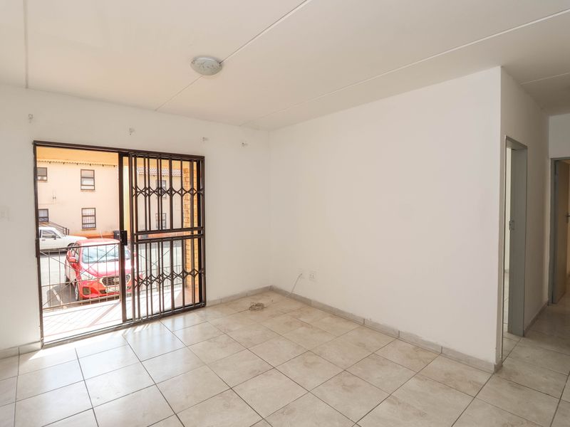 An empty, tiled living area featuring a sliding door with a security gate, providing access to the exterior.