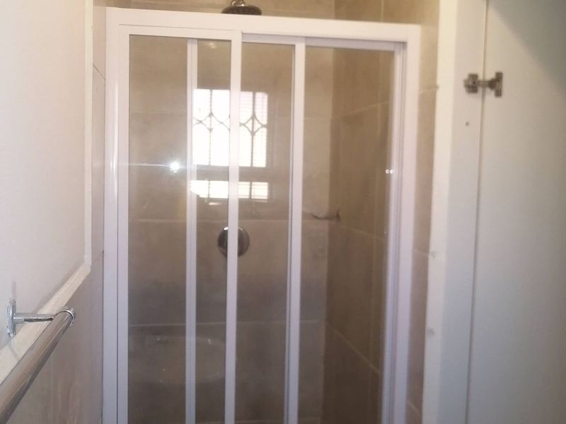 A functional bathroom featuring a shower enclosure with tiled walls, a pedestal basin, and a chrome mixer tap.