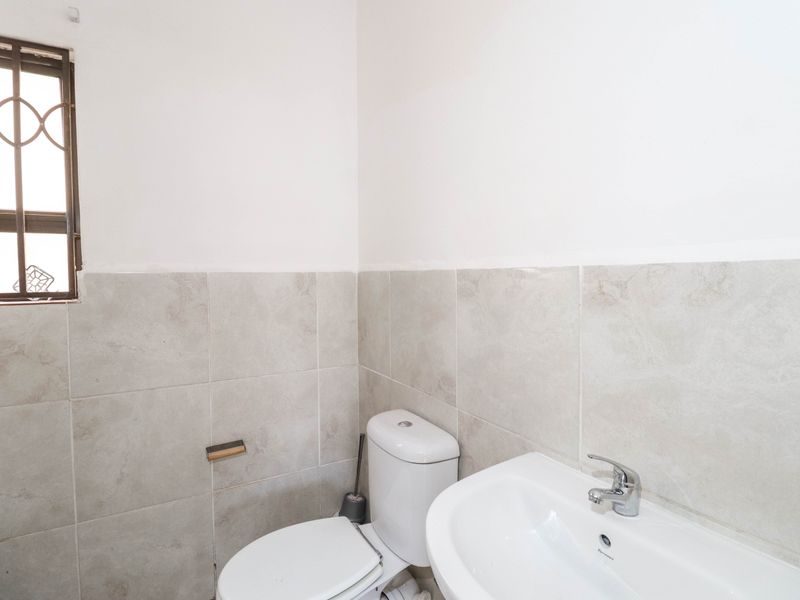 A functional bathroom featuring neutral ceramic wall tiling, a white pedestal basin with chrome mixer tap, and a standard toilet.