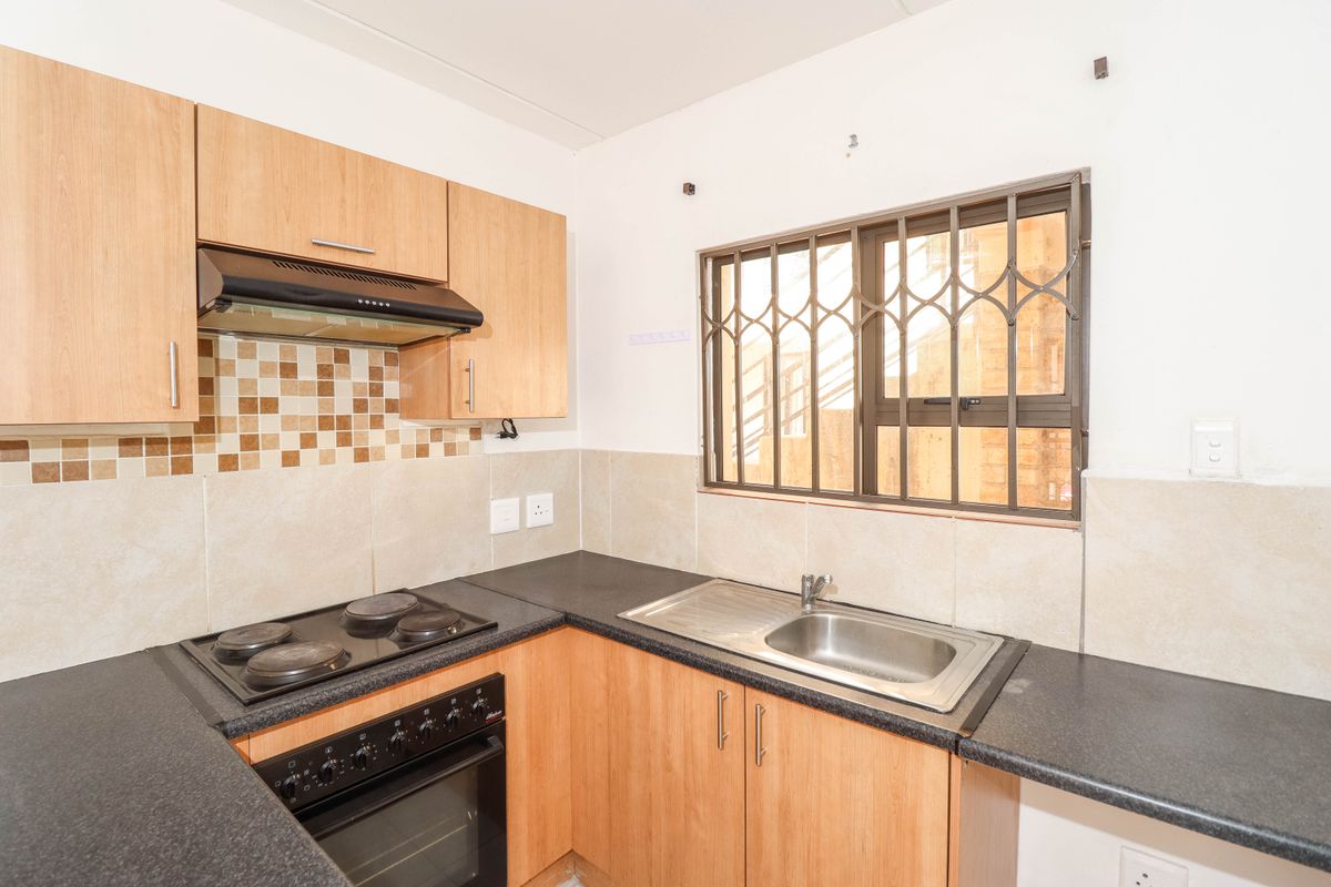 A functional kitchen featuring laminate cabinetry, dark countertops, a built-in oven with hob, and a window fitted with security bars.