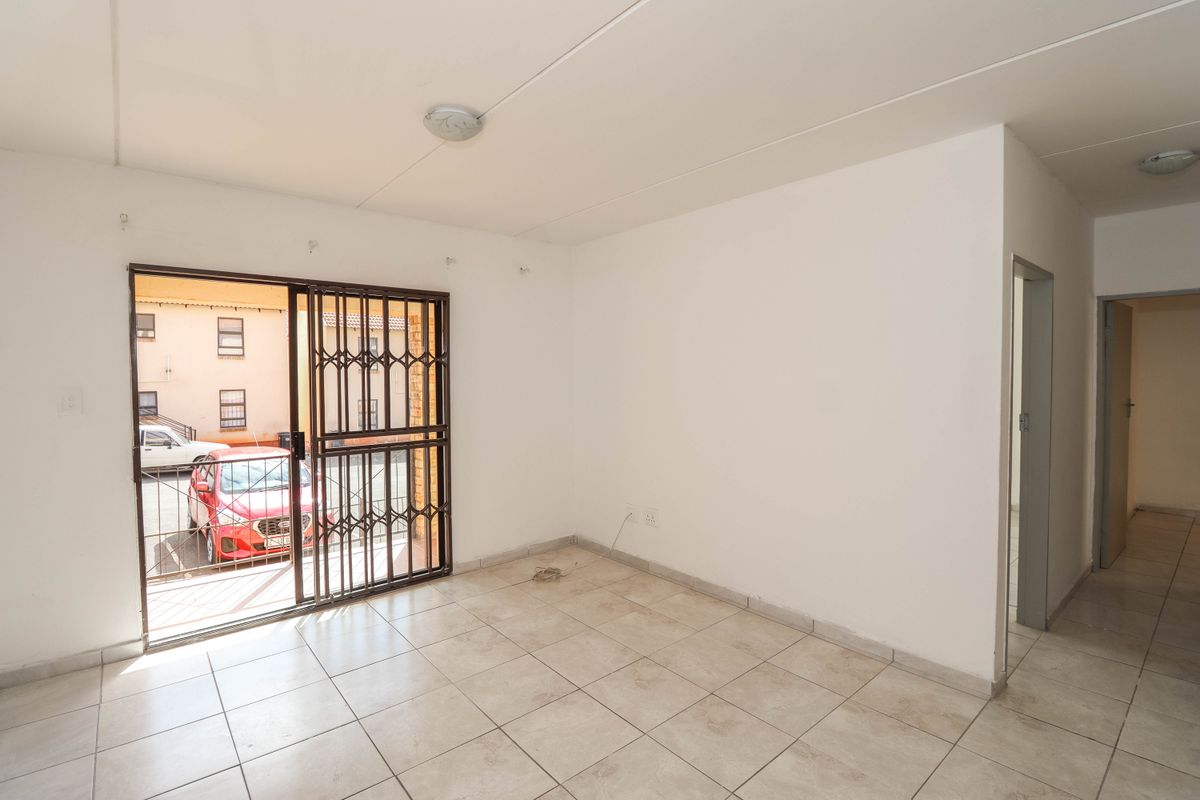 An empty, tiled living area featuring a sliding door with a security gate, providing access to the exterior.