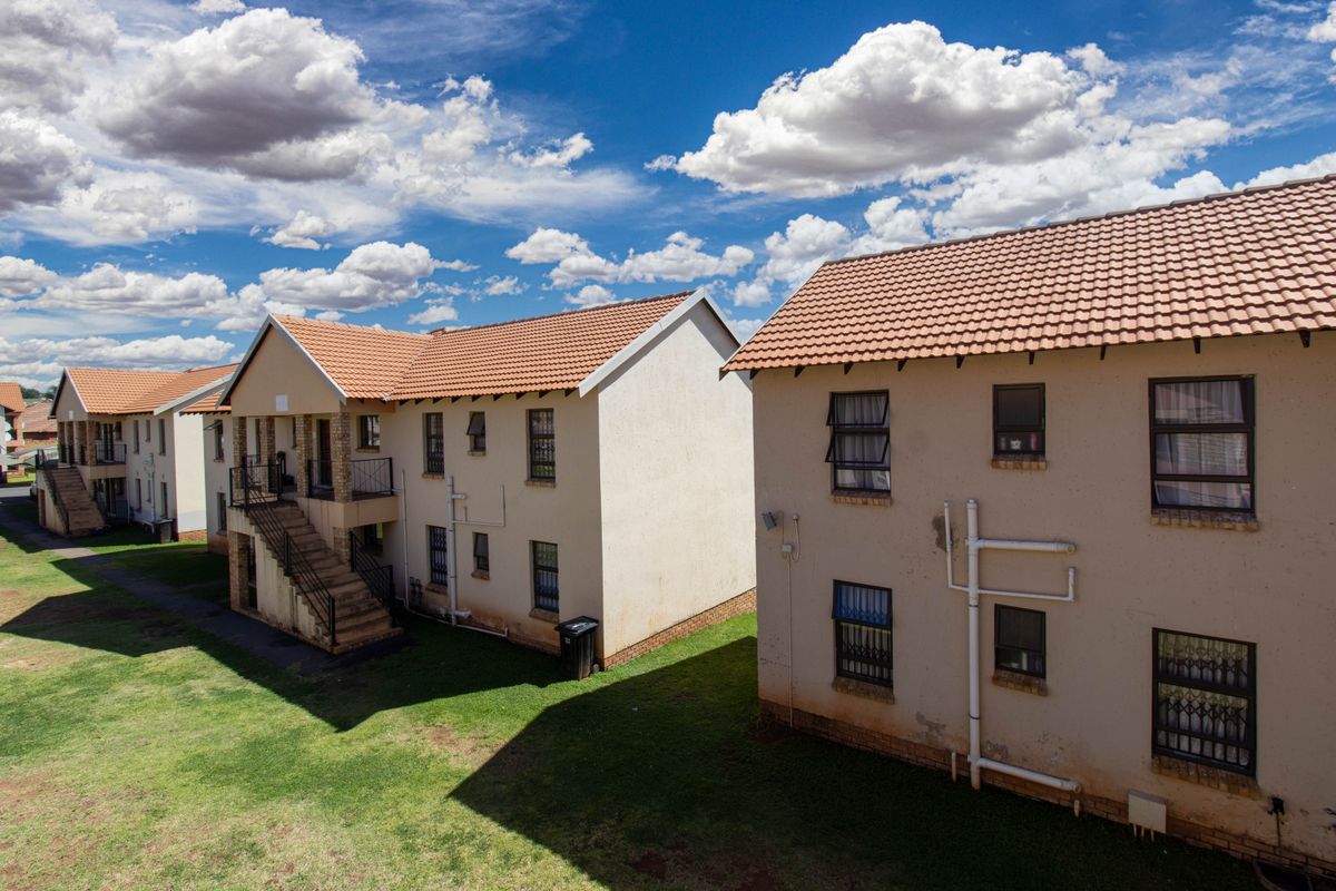 An elevated view of the apartment complex exterior, featuring tiled roofs, external staircases, and security-fitted windows with visible signs of exterior wall wear.