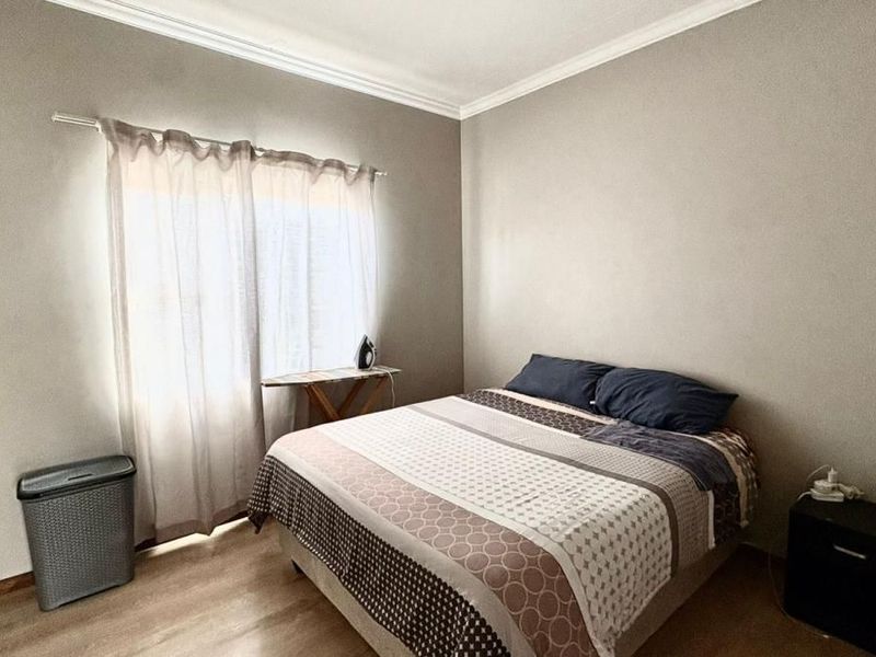 A simple bedroom featuring laminate flooring, crown molding, and a window with curtain tracks.