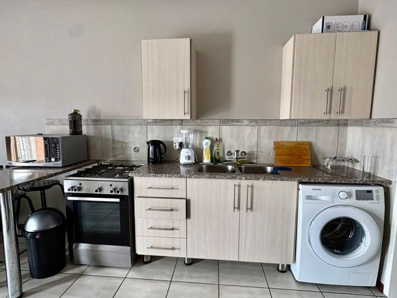 Compact kitchen featuring light wood cabinetry, granite countertops, a built-in gas stove, double sink, and integrated space for a washing machine.