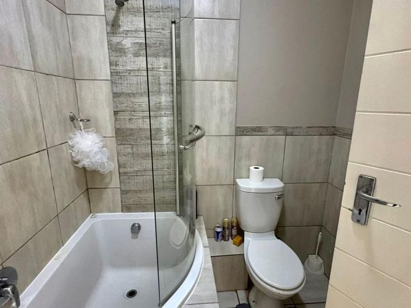 A compact bathroom featuring a curved glass shower enclosure, tiled walls with decorative accents, and a standard white toilet.