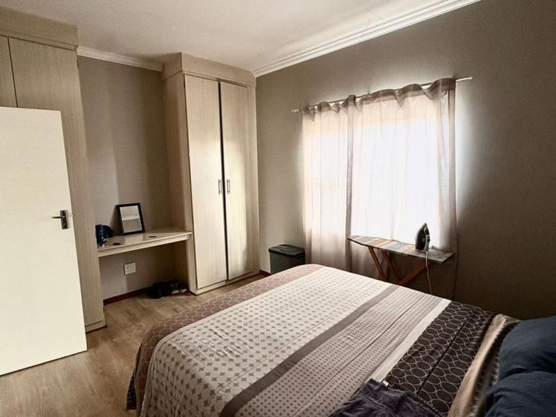A bedroom featuring built-in wooden cabinetry, a integrated desk area, and light-toned flooring, offering a functional and neutral living space.