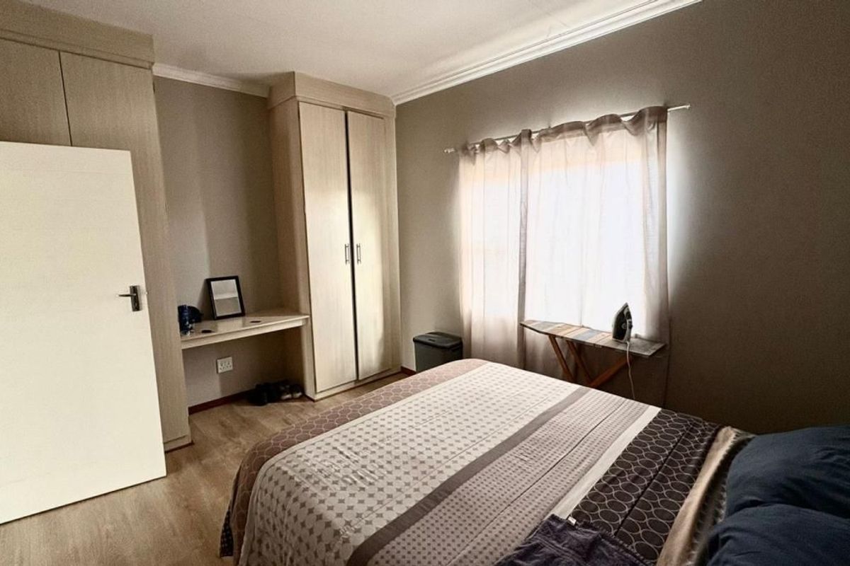 A bedroom featuring built-in wooden cabinetry, a integrated desk area, and light-toned flooring, offering a functional and neutral living space.