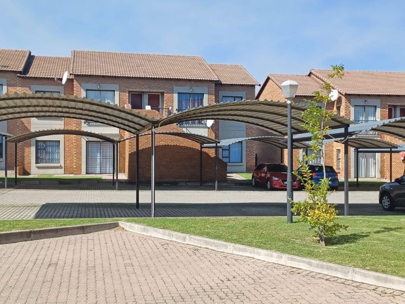 Exterior view of a residential apartment complex featuring brick facade buildings and covered parking bays with paved driveways and landscaped lawn areas.