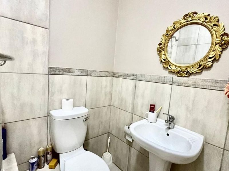 A functional bathroom featuring neutral wall tiles, a pedestal basin, a toilet, and a glass shower enclosure.