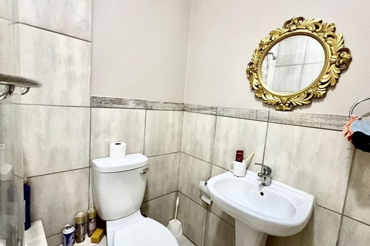 A functional bathroom featuring neutral wall tiles, a pedestal basin, a toilet, and a glass shower enclosure.