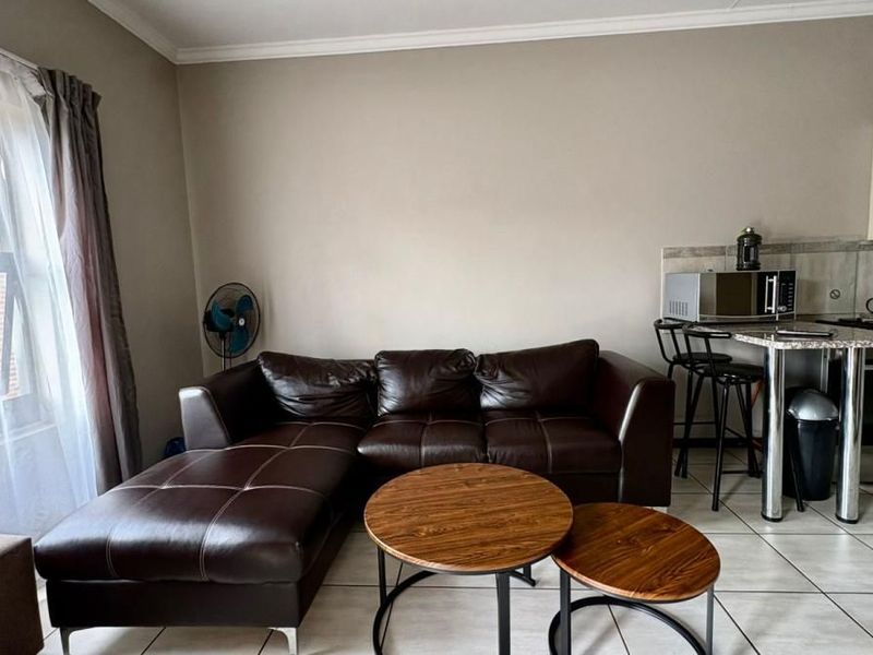 Open-plan living area featuring tiled flooring and a compact kitchen with built-in cabinetry and integrated appliances.