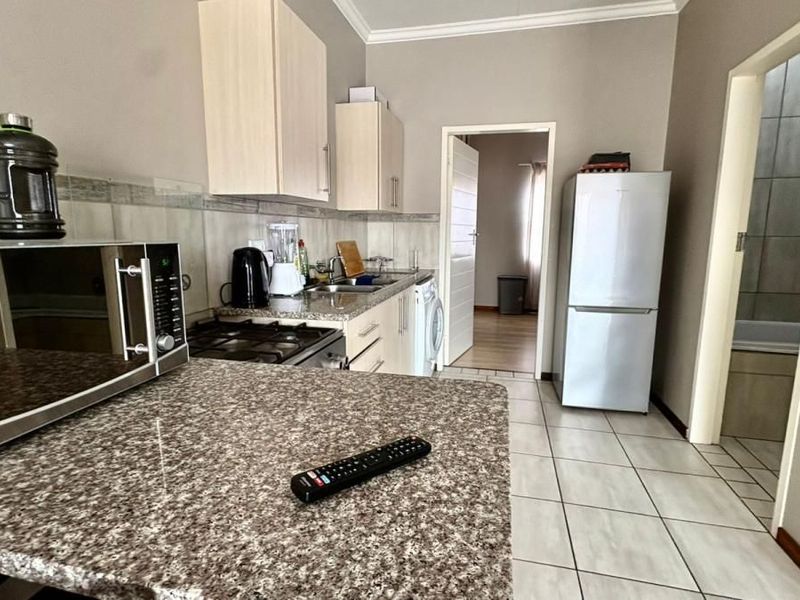 A functional kitchen featuring granite countertops, light-toned cabinetry, tiled flooring, and a built-in gas hob, with direct access to adjacent living and bathroom areas.