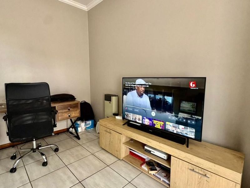 A functional living area featuring tiled flooring, neutral wall tones, and built-in cabinetry, currently utilized as a combined lounge and workspace.