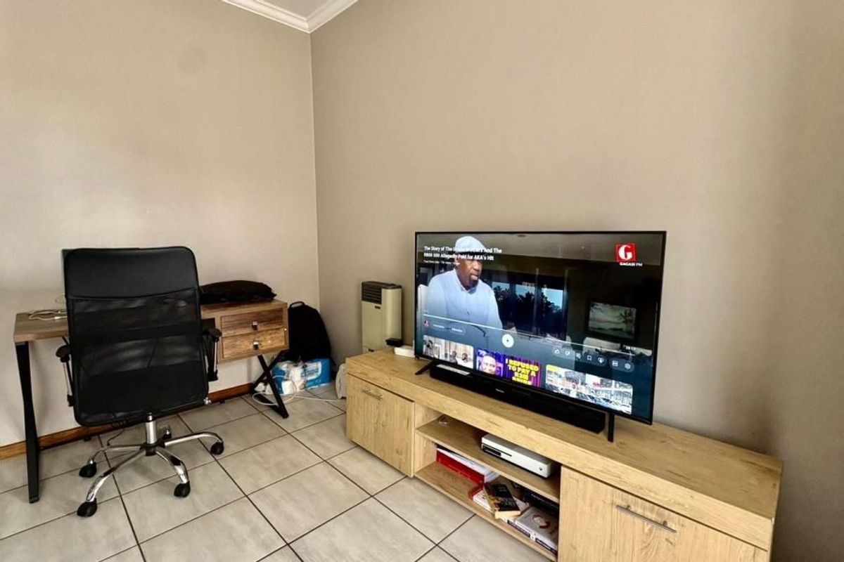 A functional living area featuring tiled flooring, neutral wall tones, and built-in cabinetry, currently utilized as a combined lounge and workspace.