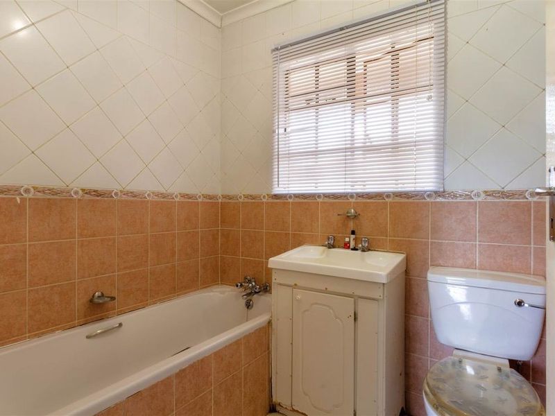 A dated bathroom featuring a bathtub, vanity basin, and toilet with tiled walls and a window blind.