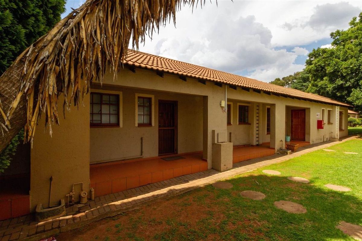 Rear view of an apartment building featuring a long covered patio, tiled flooring, and access to a shared garden area.